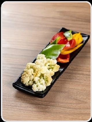 Buquês de couve-flor ao lado de tiras de pimentão amarelo, vermelho e verde, na travessa preta