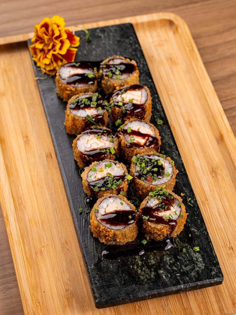 Hot rolls empanados cobertos de molho tarê escuro e cebolinha, na ardósia
