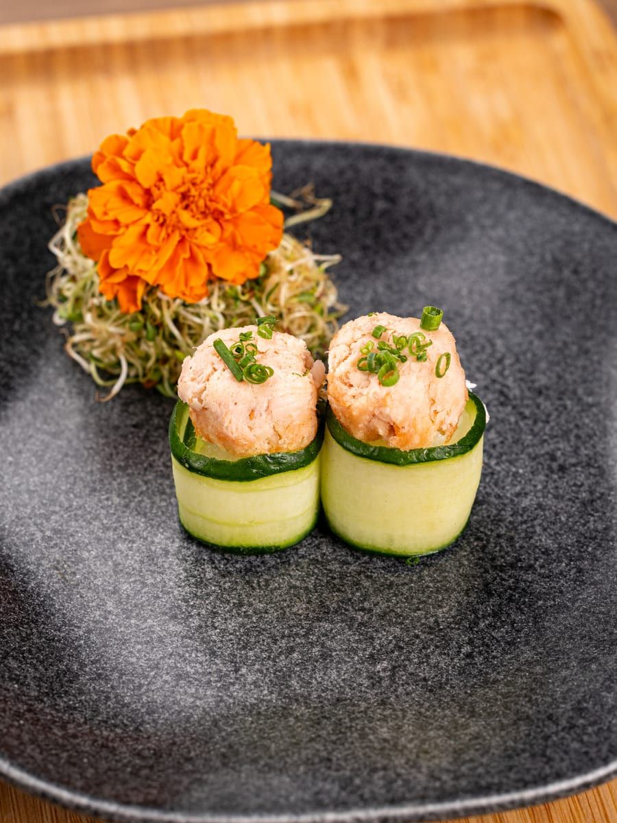 Dois bolinhos de patê de salmão com cebolinha, enrolados em lâminas de pepino, no prato preto