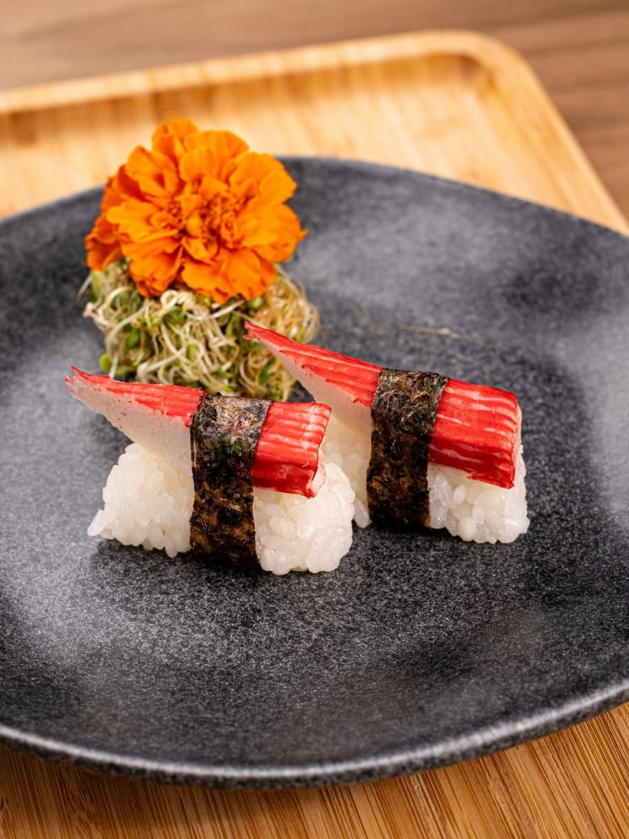 Dois niguiris de kani com cinta de alga nori, no prato preto