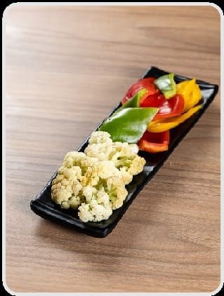Tiras de pimentão amarelo, vermelho e verde ao lado de buquês de couve-flor, na travessa preta