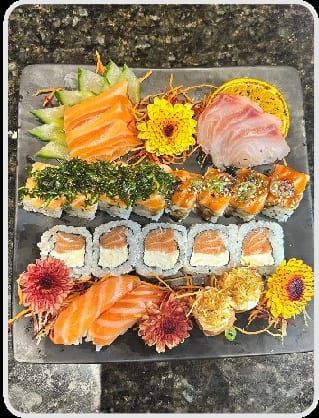 Travessa grande de pedra com fileiras de sashimi, uramaki e niguiri, decorada com flores comestíveis