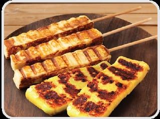 Espetos de queijo coalho grelhado, com marcas escuras da grelha, sobre tábua de madeira