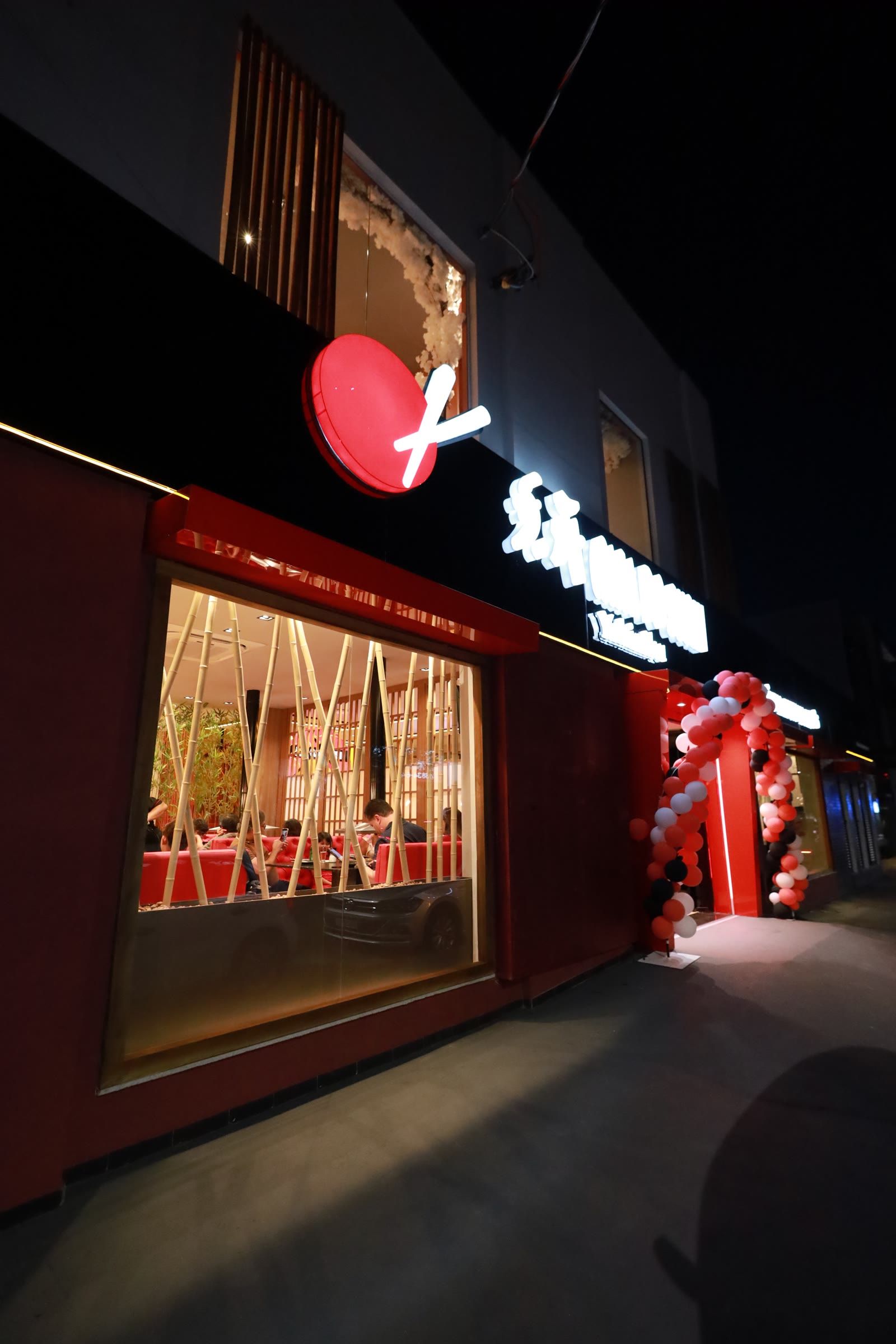 Fachada à noite, com o logo vermelho aceso no painel preto e a vitrine iluminada