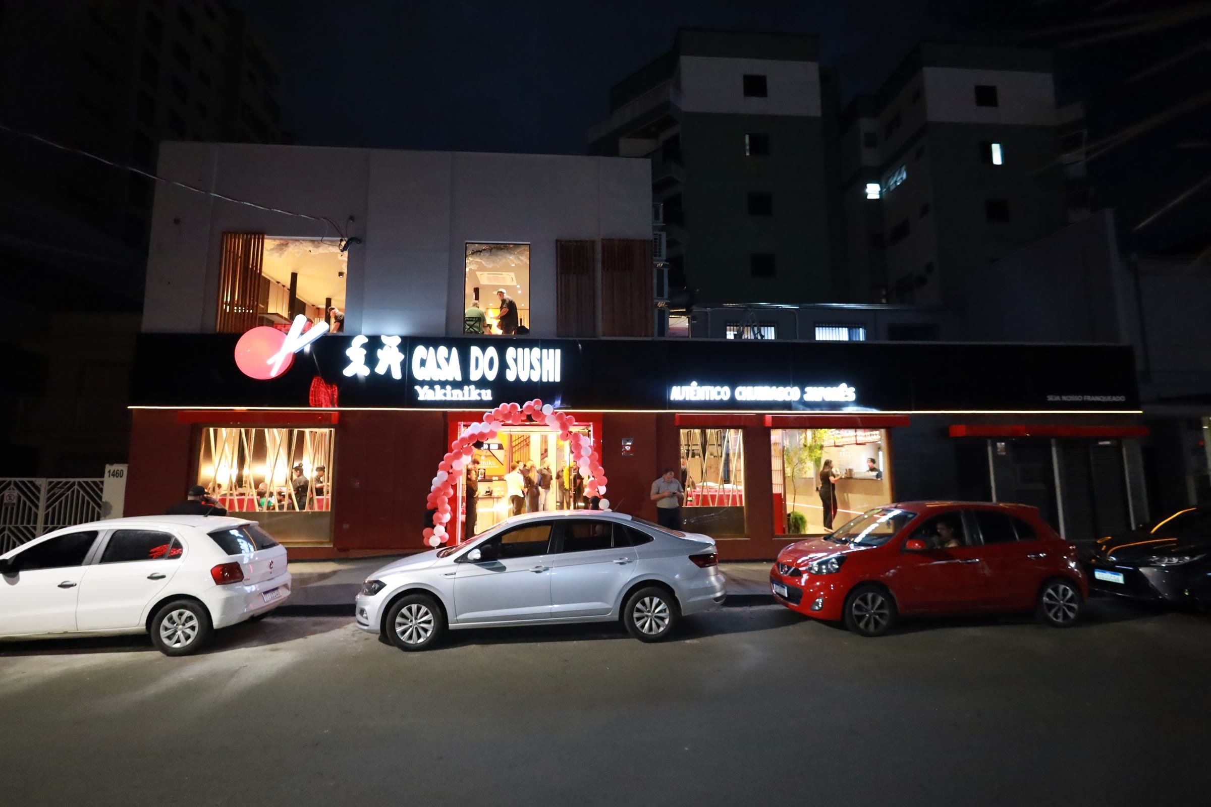 Fachada do restaurante à noite, com o letreiro iluminado e carros estacionados na rua