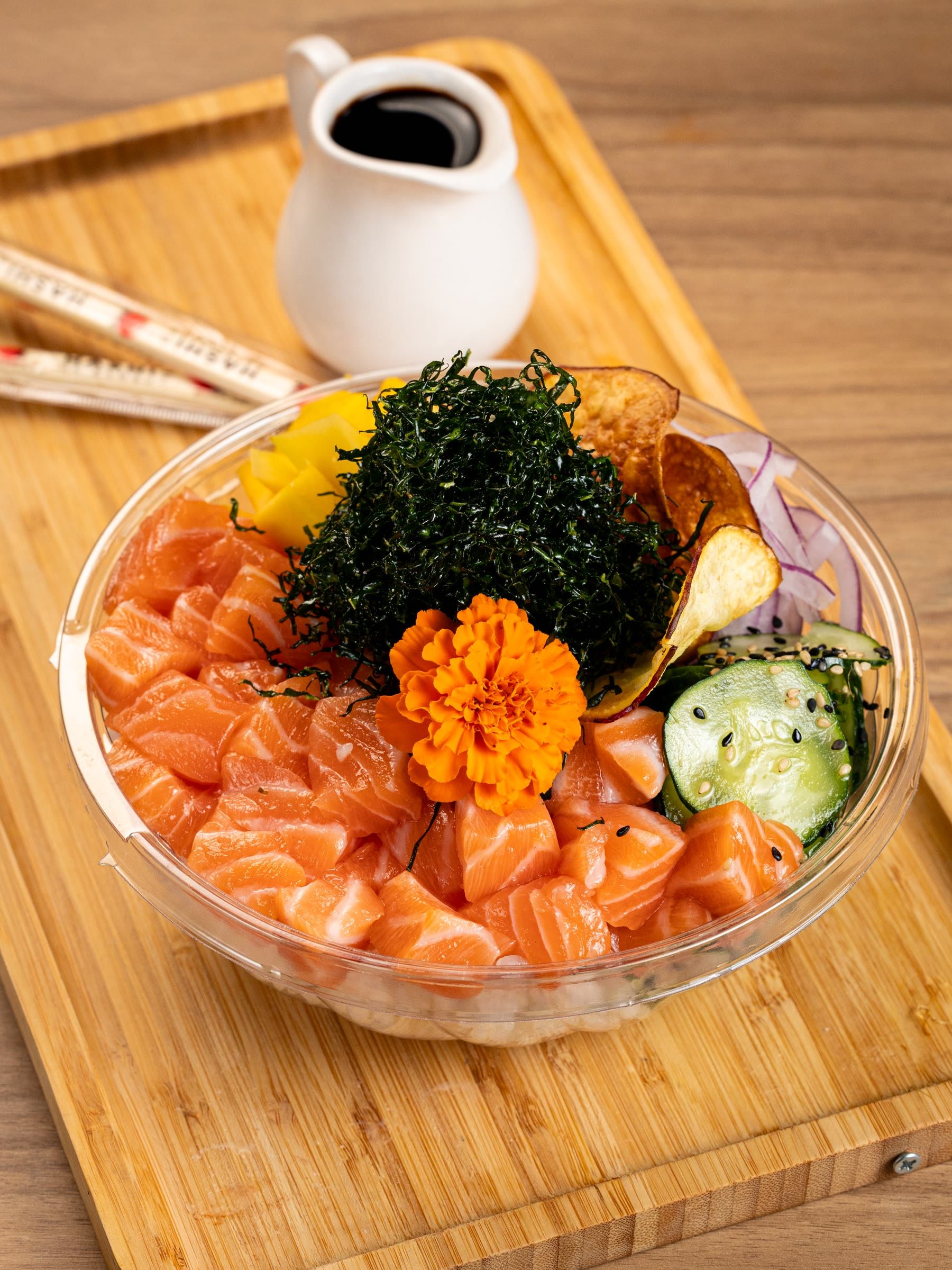 Poke farto de salmão cru com nori, manga e flor comestível no bowl sobre tábua de bambu