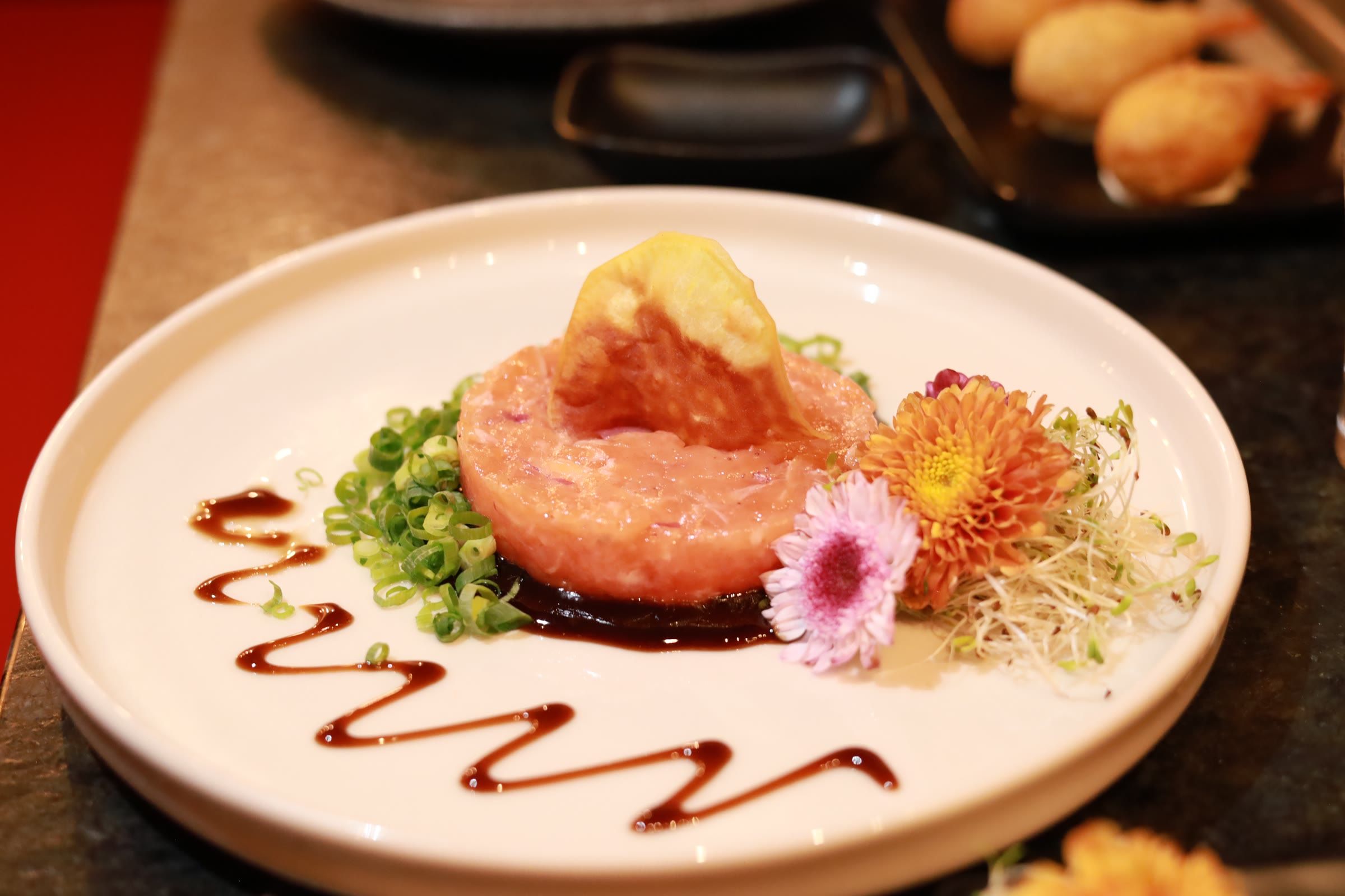 Tartar de salmão em anel com tempura dourada por cima, flores comestíveis e risco de molho