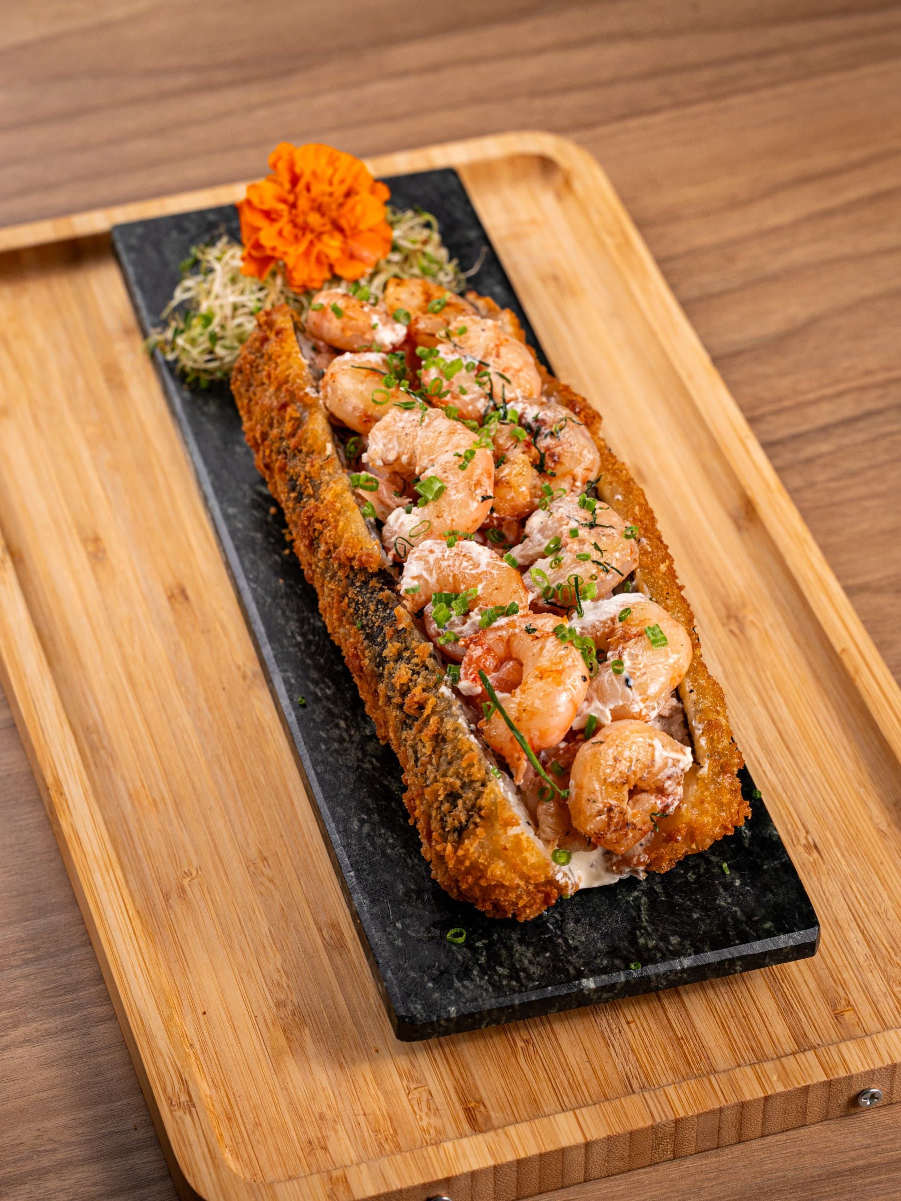 Big hot roll empanado coberto de camarão e cebolinha, servido em ardósia sobre tábua de bambu