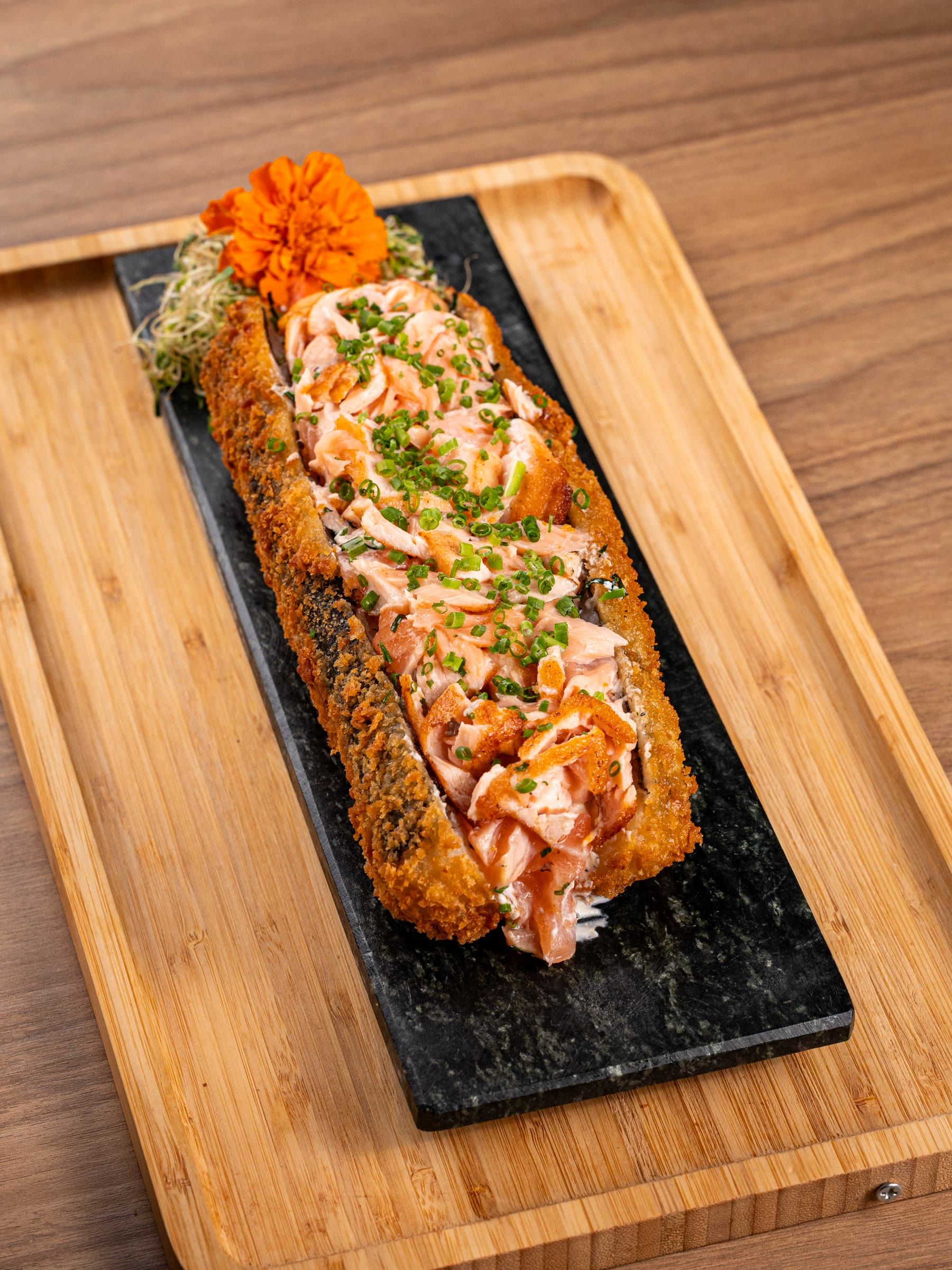 Big hot roll com salmão grelhado maçaricado e maionese, em ardósia sobre tábua de bambu