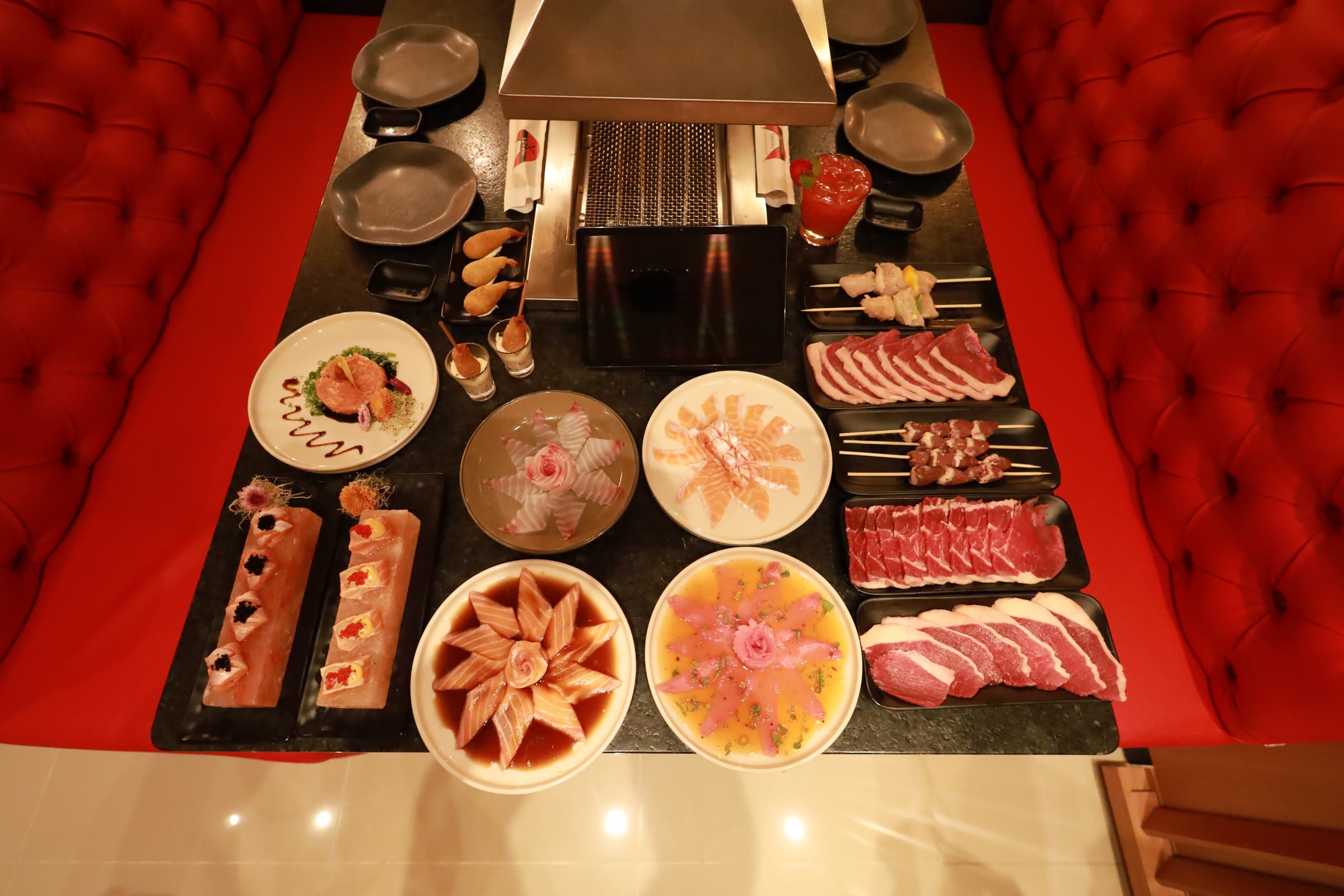 Sushi, carpaccio e bandejas de carne crua ao redor da grelha embutida na mesa