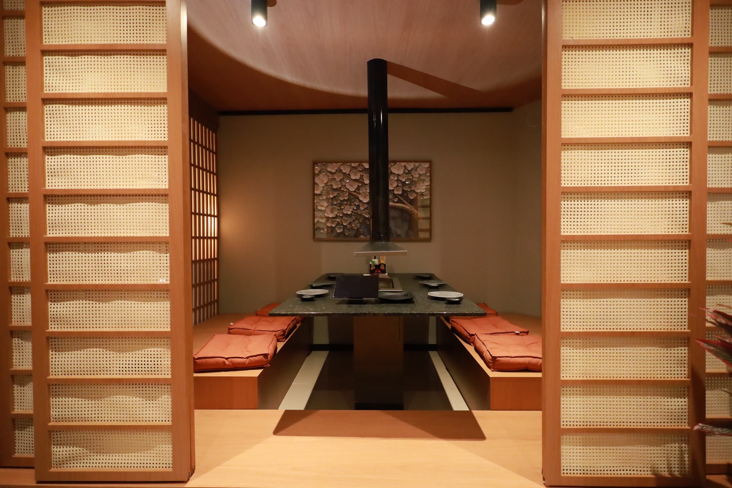 Sala privativa em tatame atrás das portas shoji, com mesa rebaixada de grelha e almofadas laranja