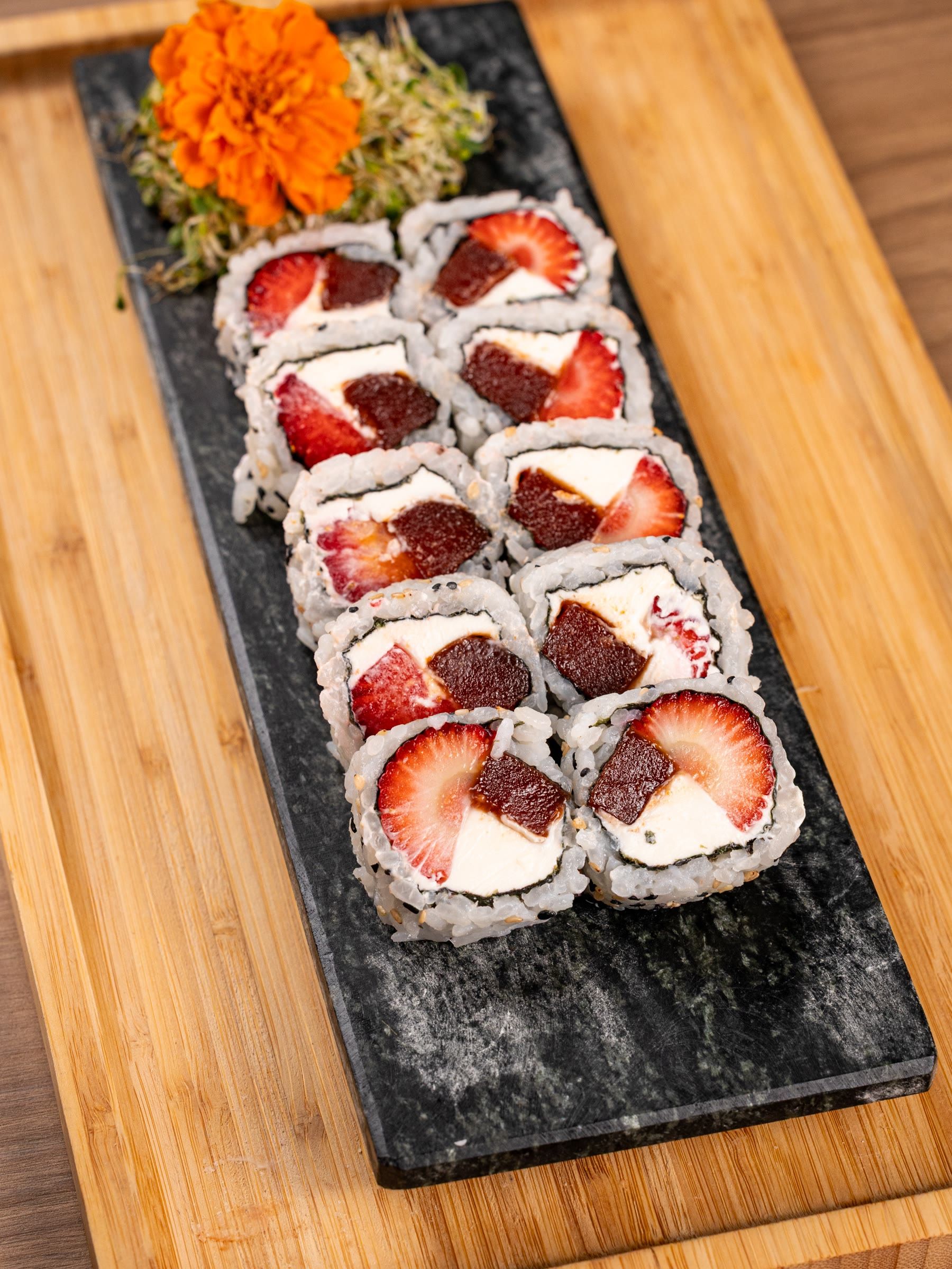 Duas fileiras de uramaki com cream cheese, goiabada e morango fatiado sobre ardósia preta