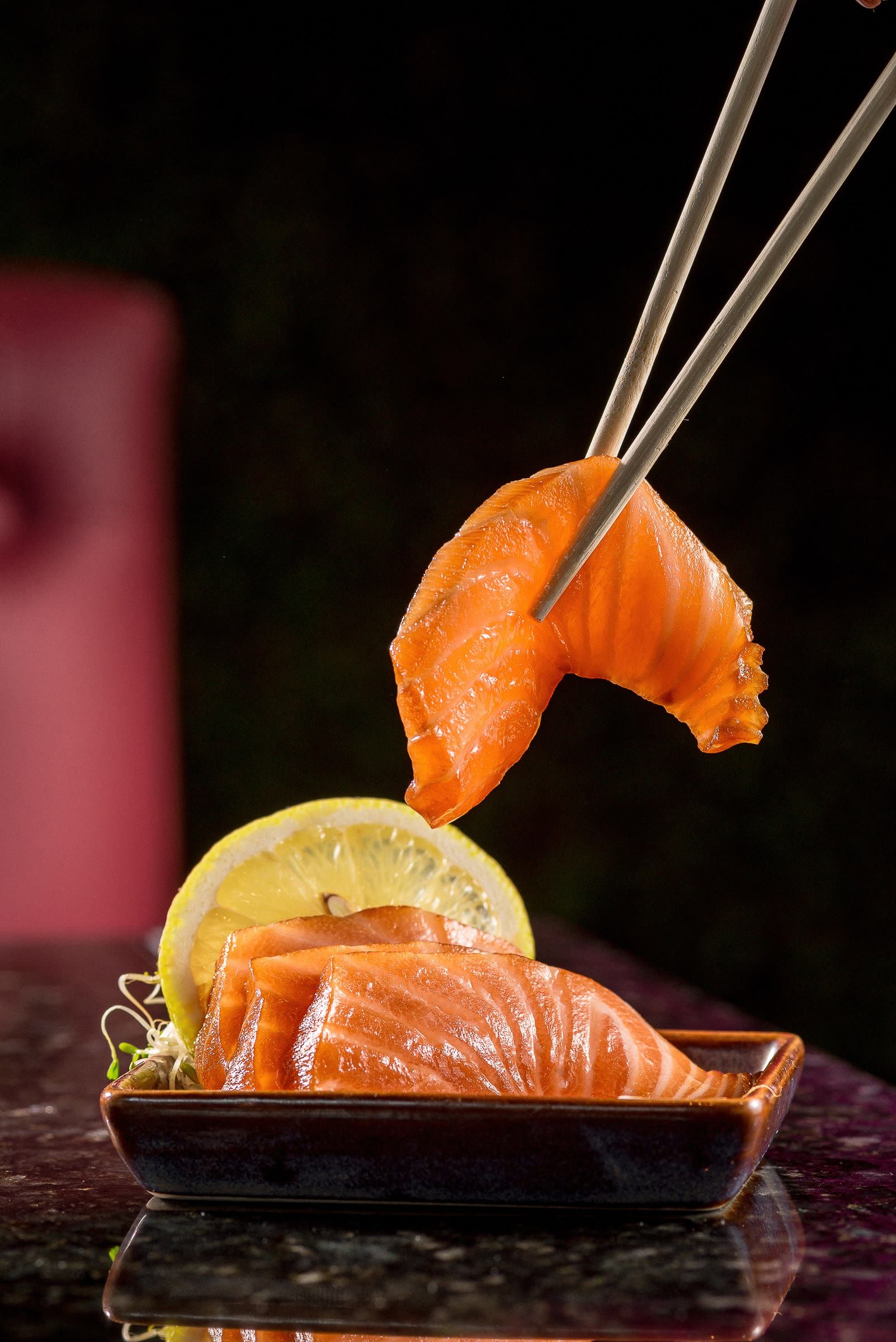 Hashi de metal erguendo uma fatia de salmão sobre a barquinha de sashimi