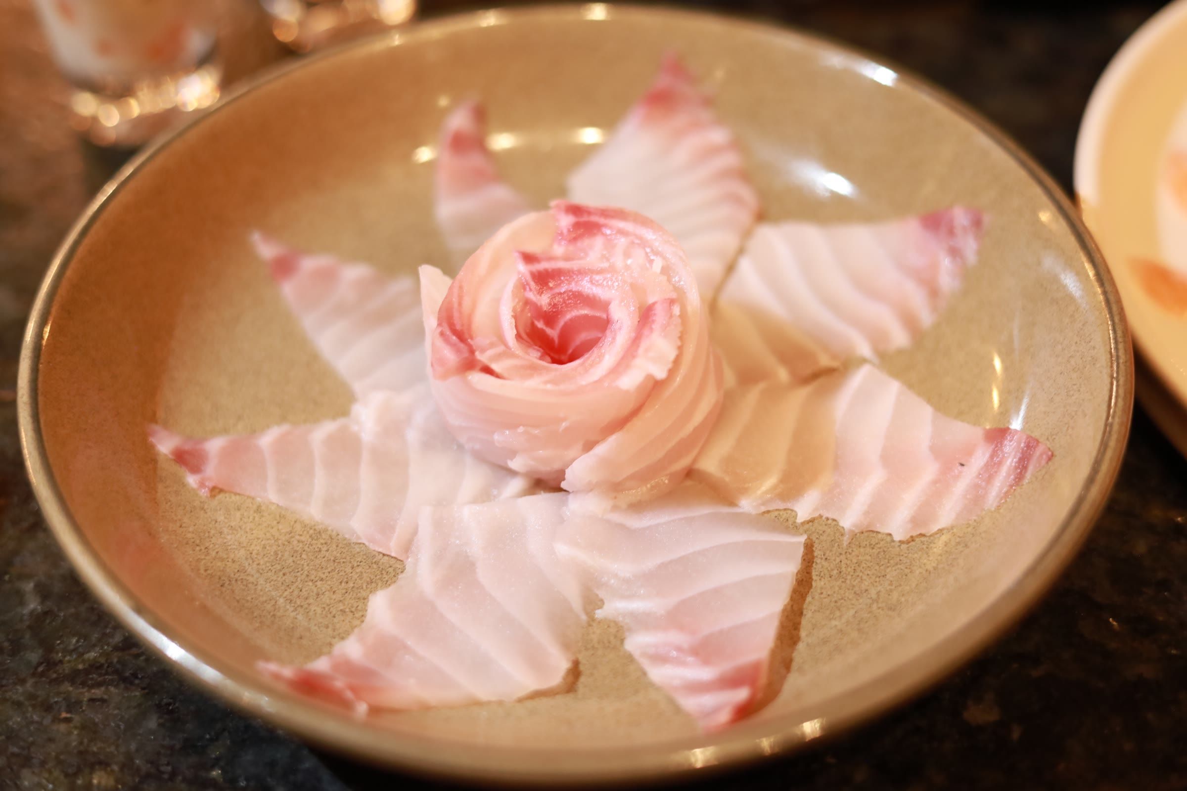 Fatias finas de peixe branco arranjadas em forma de flor sobre prato dourado
