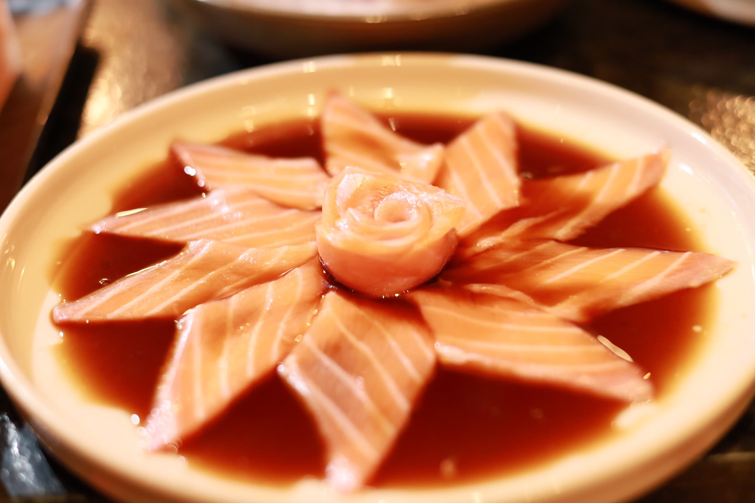 Sashimi de salmão arranjado em flor sobre molho shoyu escuro, com rosa de peixe no centro
