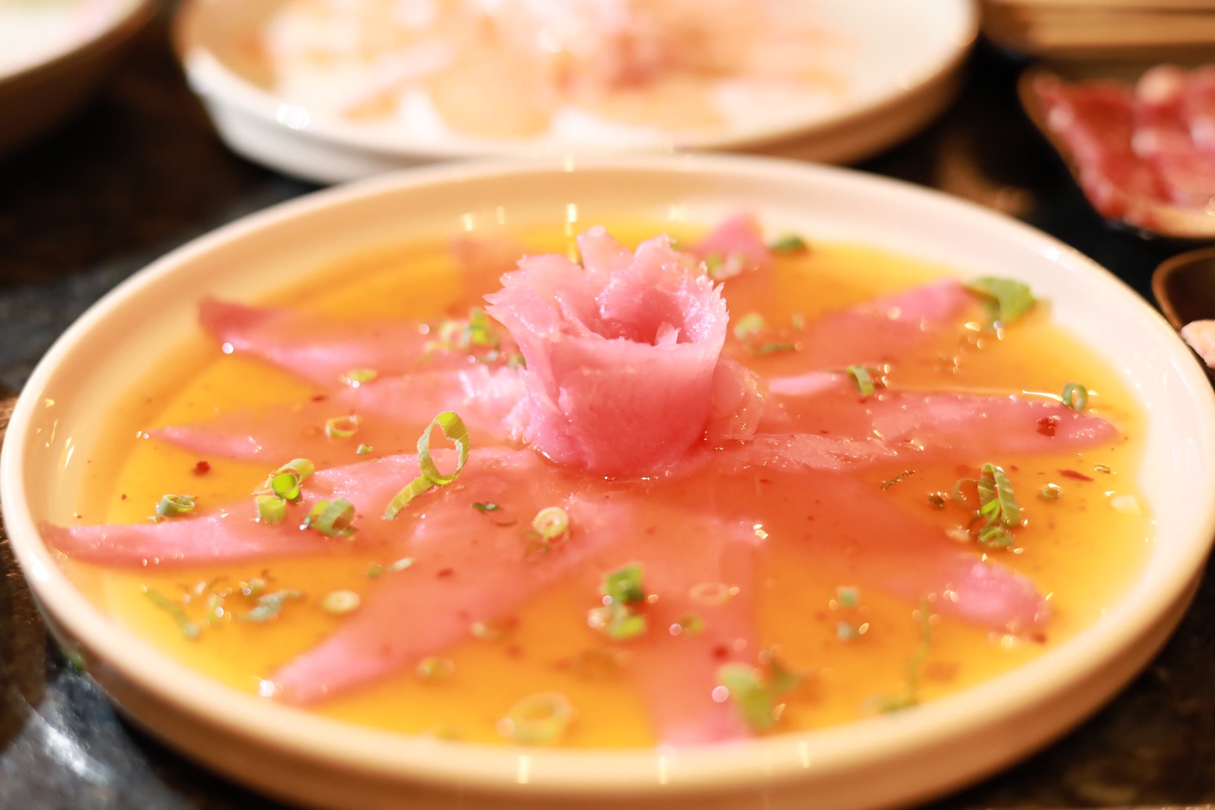 Carpaccio de salmão com molho alaranjado, cebolinha e rosa de peixe ao centro do prato