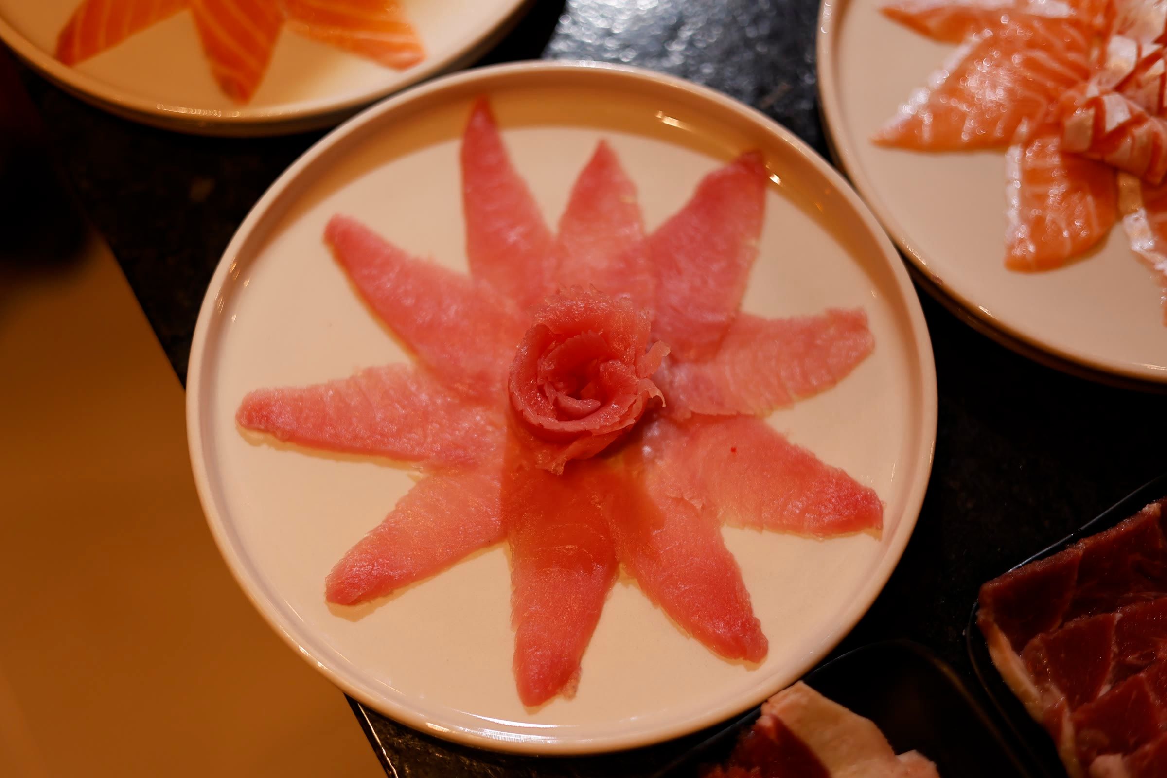Três pratos de sashimi de peixe branco e salmão saindo do balcão