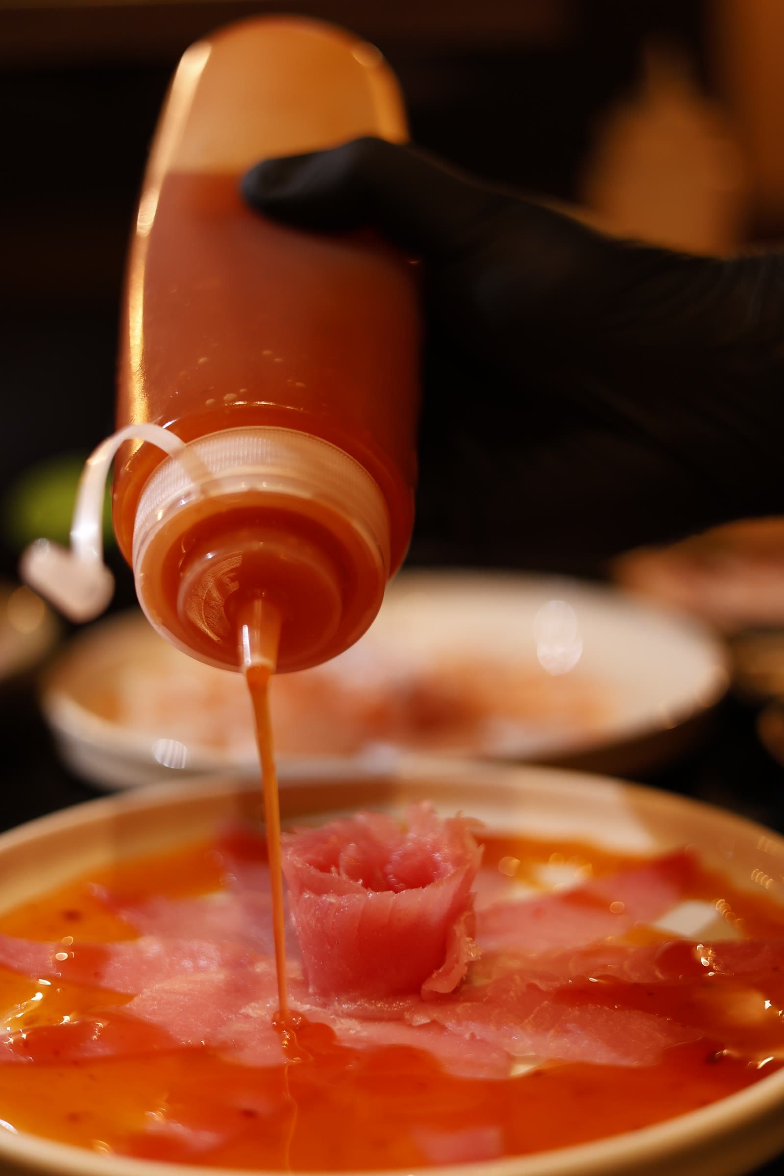 Filete de molho alaranjado caindo da bisnaga direto na rosa de peixe cru do prato