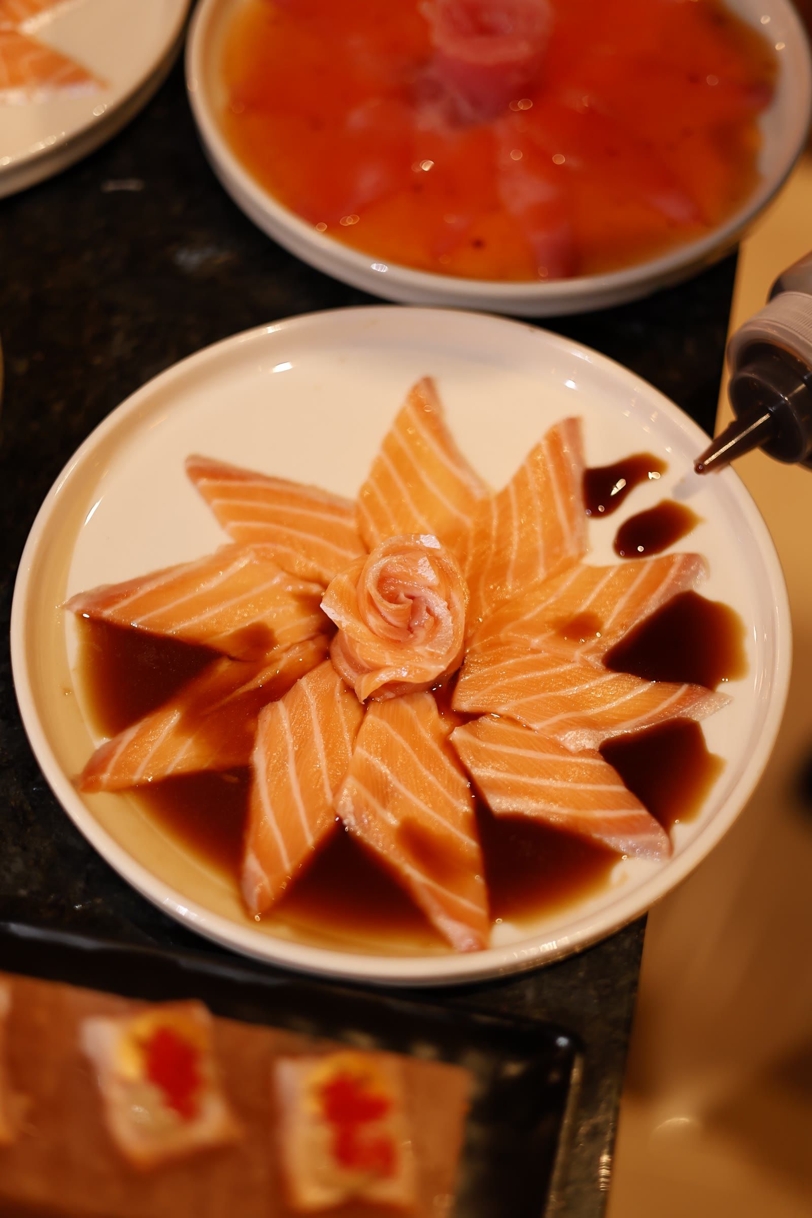 Bisnaga pingando shoyu no prato de salmão em flor, com a bandeja de niguiris embaixo