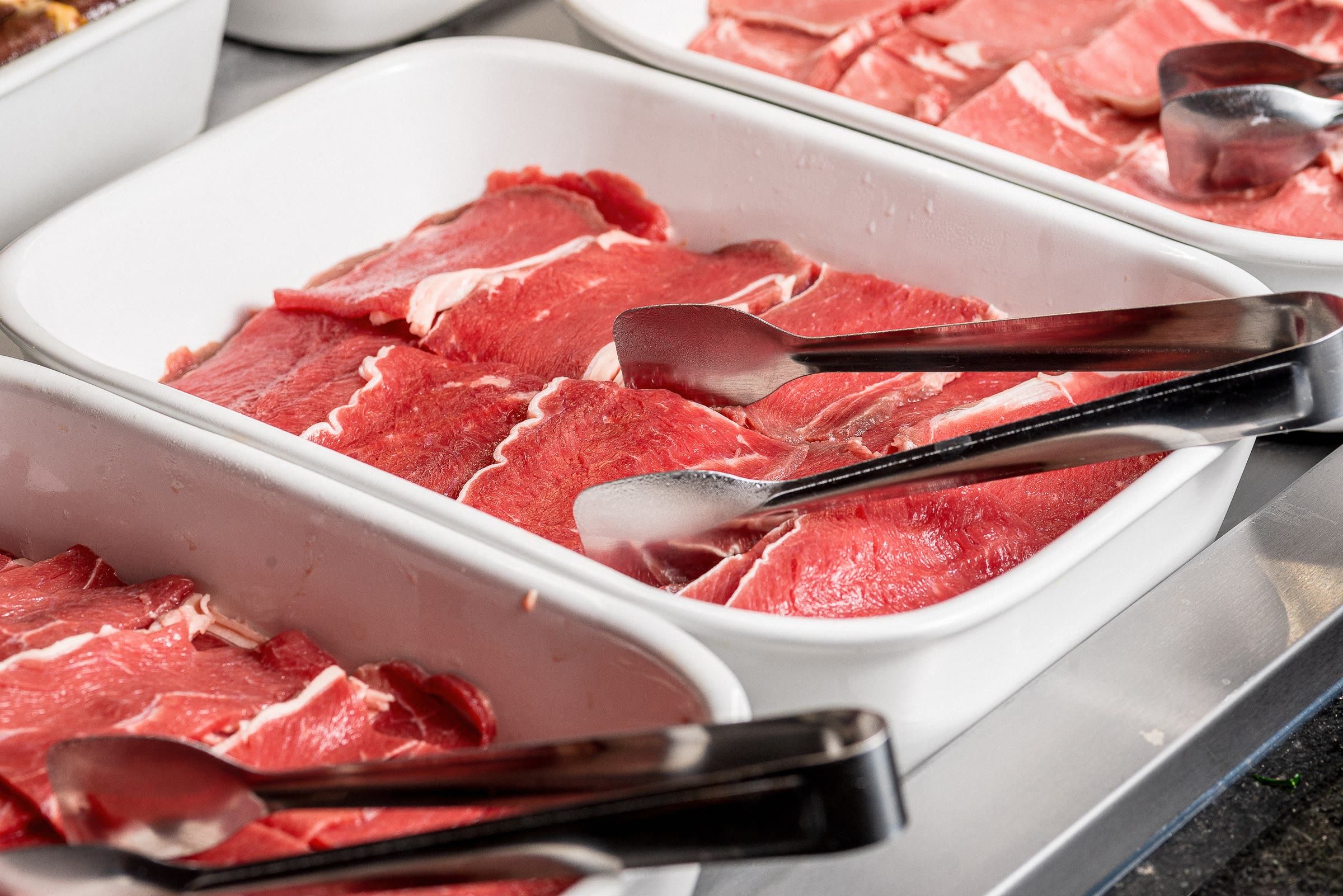 Fatias finas de carne marmorizada na bandeja, prontas para o garçom levar à sua mesa