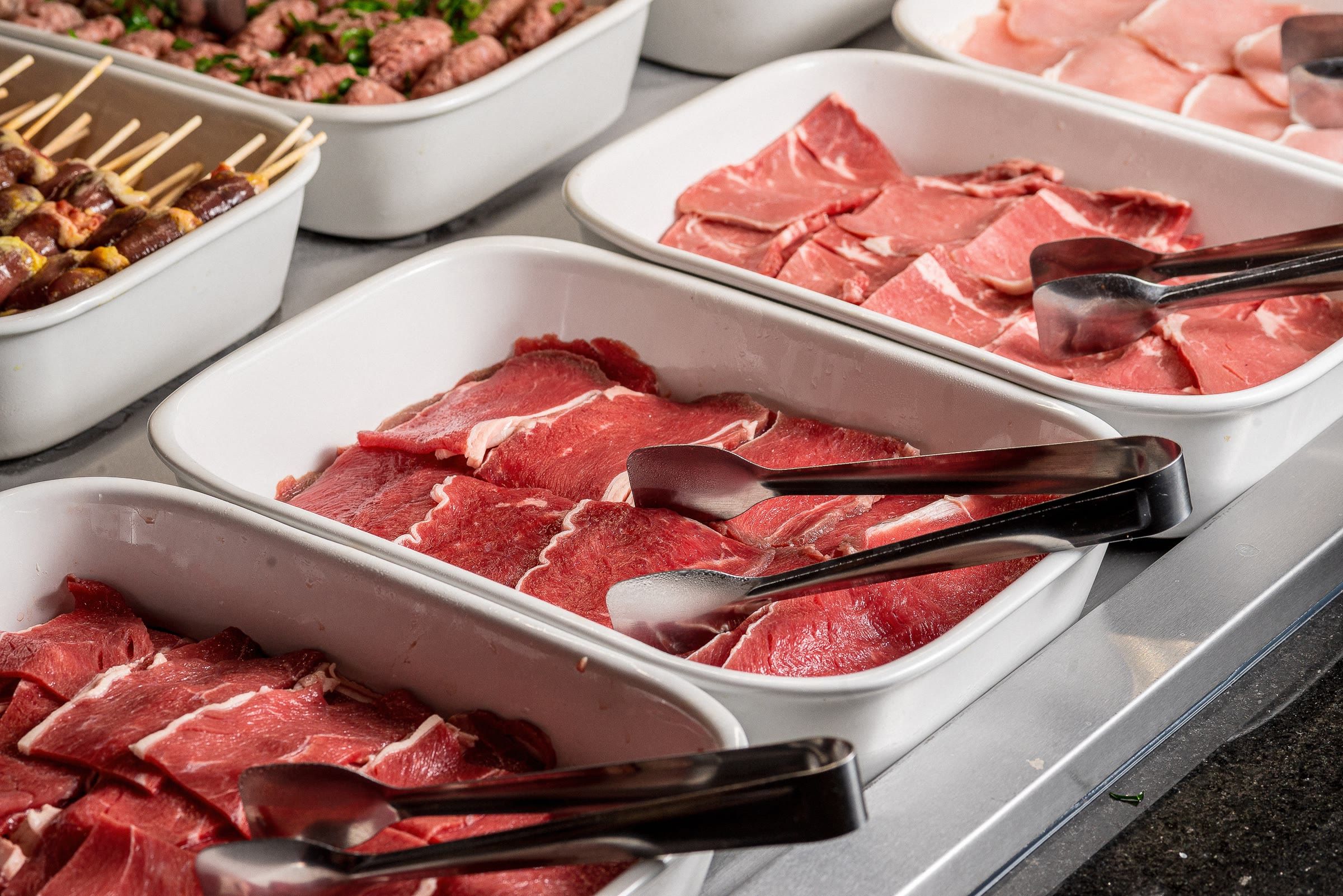 Bandejas de carne crua fatiada e espetinhos temperados no balcão de serviço da casa