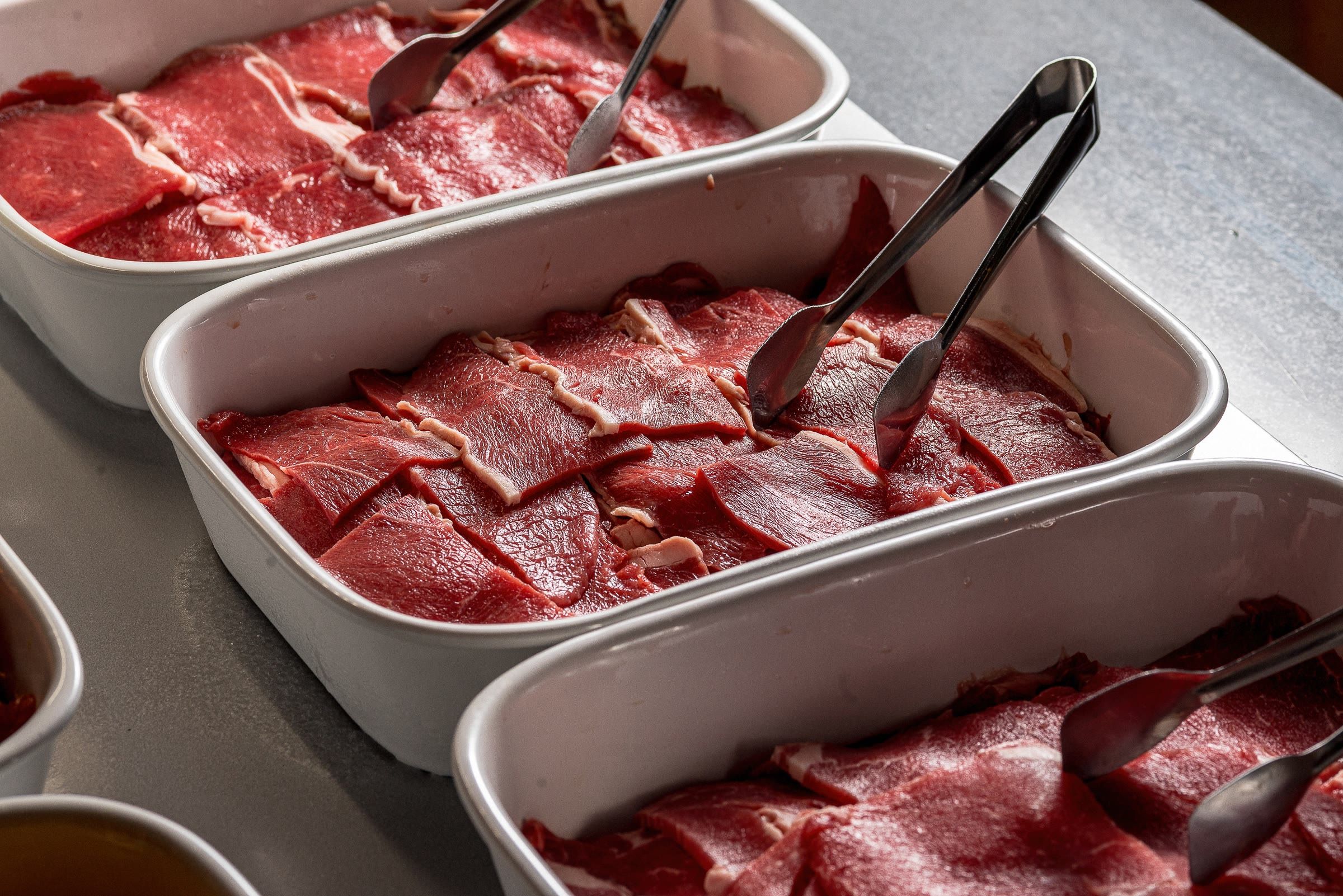 Três cubas alinhadas de carne bovina fatiada na hora, prontas para seguir para as mesas