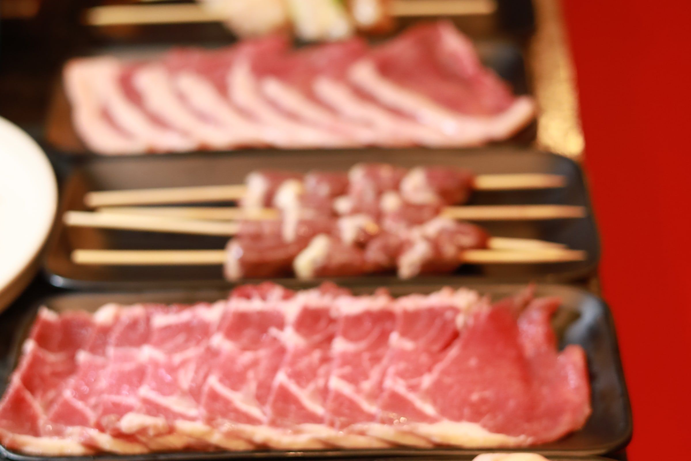 Bandeja preta com fatias finas de carne crua enfileiradas e espetinhos de frango montados, prontos para a grelha