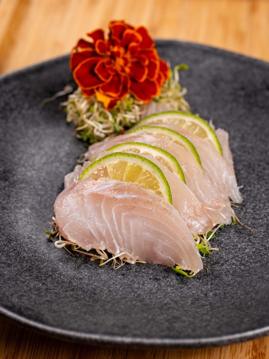 Fatias finas de peixe branco intercaladas com rodelas de limão, no prato preto