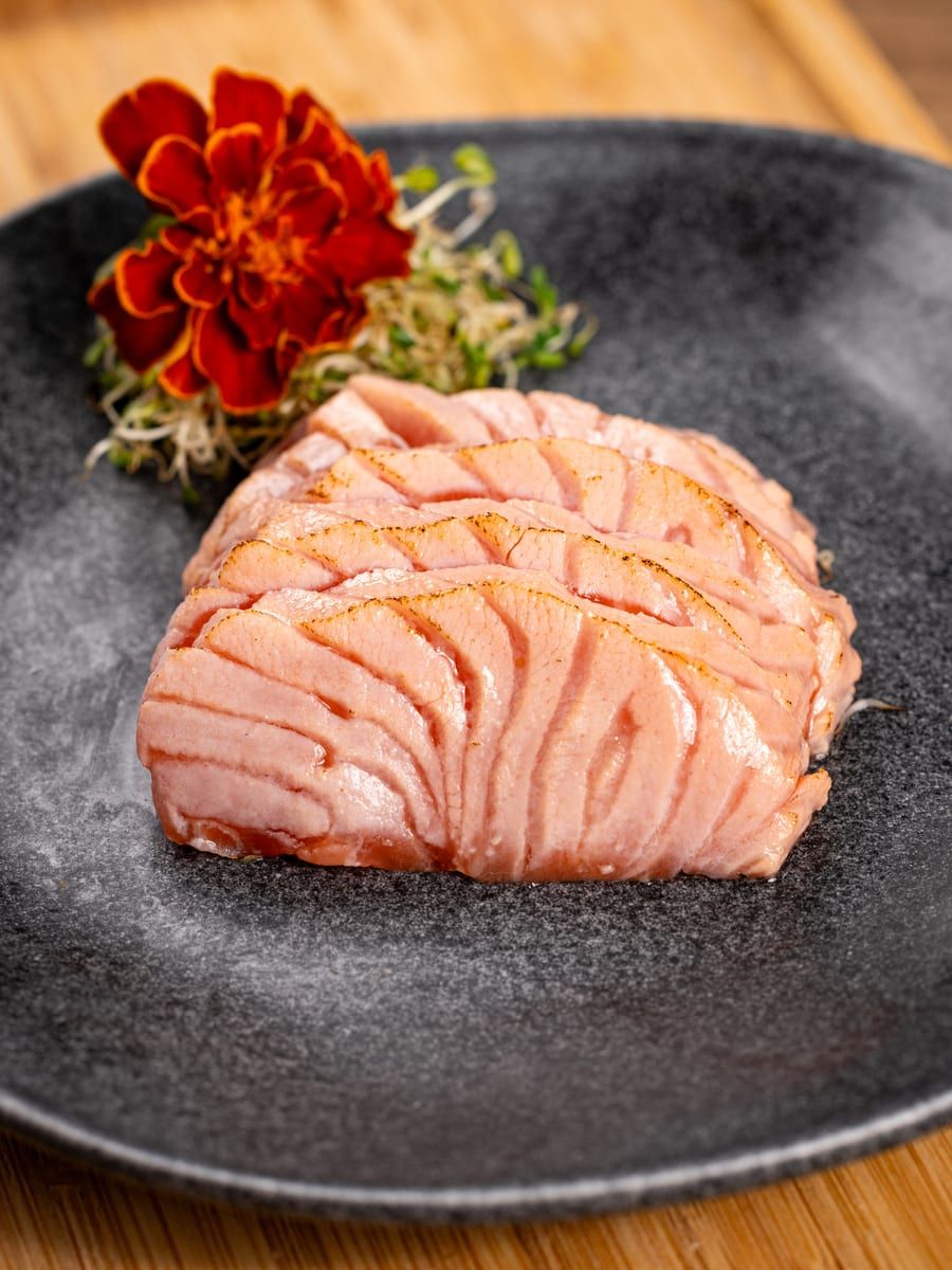 Fatias de salmão maçaricado, douradas na superfície, enfileiradas no prato preto