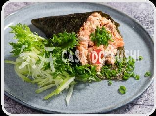 Cone de alga aberto em prato cinza, recheado de salmão picado com cebolinha, ao lado de folhas verdes